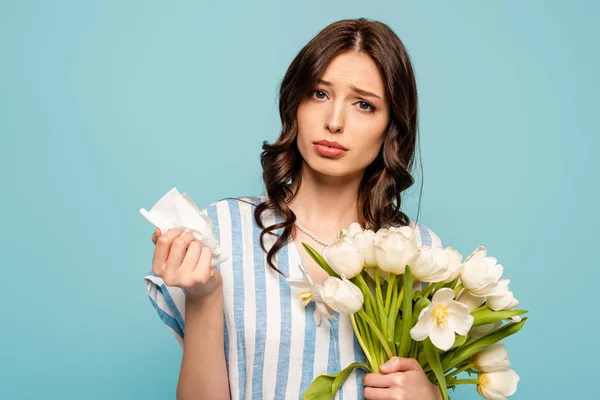 Malattie giovane donna in possesso di tovagliolo di carta e bouquet di tulipani bianchi isolati su blu — Foto stock