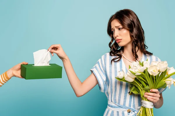 Cropped view of woman giving paper napkins to upset, sick girl with bouquet of white tulips isolated on blue — Stock Photo