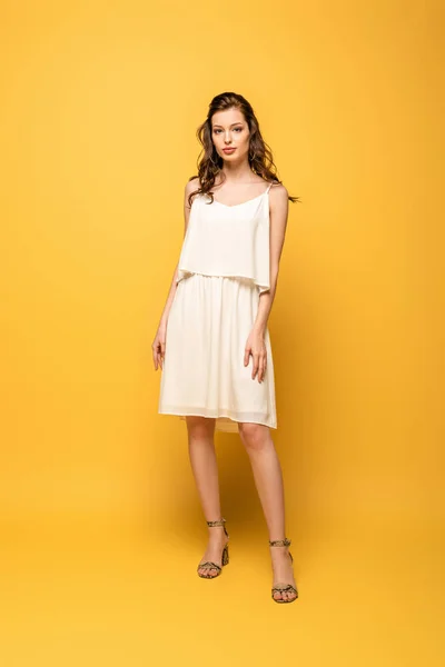 Full length view of beautiful, confident young woman looking at camera while standing on yellow background — Stock Photo