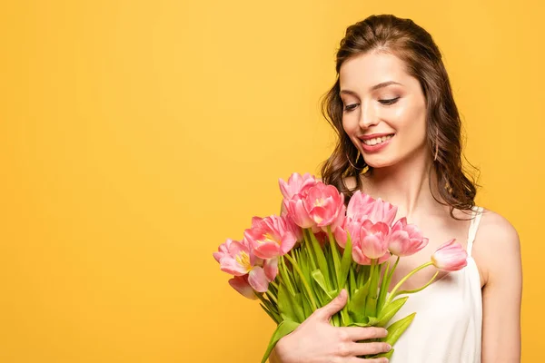 Felice giovane donna che tiene bouquet di tulipani rosa isolati su giallo — Foto stock