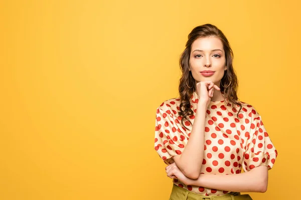 Atraente jovem mulher de mão perto do queixo, enquanto sorrindo para a câmera isolada no amarelo — Fotografia de Stock