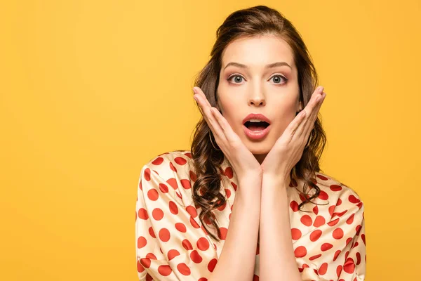 Scioccato giovane donna guardando la fotocamera mentre si tiene le mani vicino al viso isolato sul giallo — Foto stock