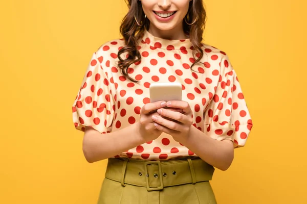 Обрізаний вид молодої жінки, яка посміхається під час спілкування на смартфоні ізольовано на жовтому — стокове фото