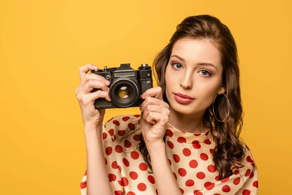 Selbstbewusste junge Frau mit Digitalkamera, während sie die Kamera isoliert auf gelb betrachtet — Stockfoto