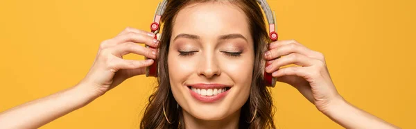 Panoramic shot of happy young woman listening music in wireless headphones with closed eyes isolated on yellow — Stock Photo