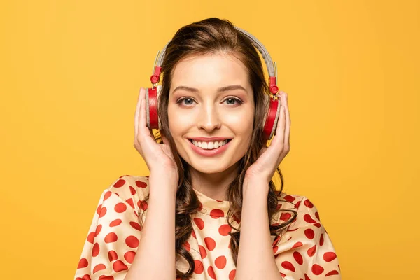 Щаслива молода жінка торкається навушників, посміхаючись на камеру ізольовано на жовтому — стокове фото