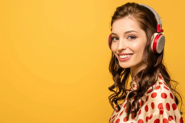 Happy young woman in wireless headphones smiling at camera isolated on yellow — Stock Photo