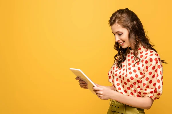 Mujer joven sonriendo mientras usa tableta digital aislada en amarillo - foto de stock