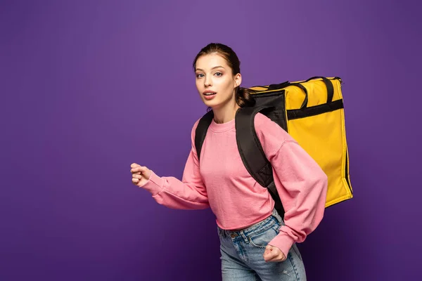 Attraente corriere in esecuzione mentre trasporta la scatola termica e guardando la fotocamera isolata su viola — Foto stock