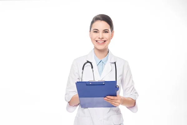 Schöne Ärztin lächelt in die Kamera, während sie auf Klemmbrett auf weiß isoliert schreibt — Stockfoto