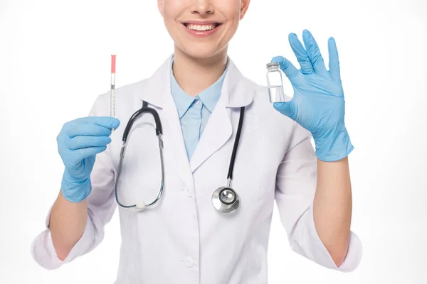 Vista recortada del médico sonriente sosteniendo la jeringa y el frasco con la vacuna aislada en blanco — Stock Photo