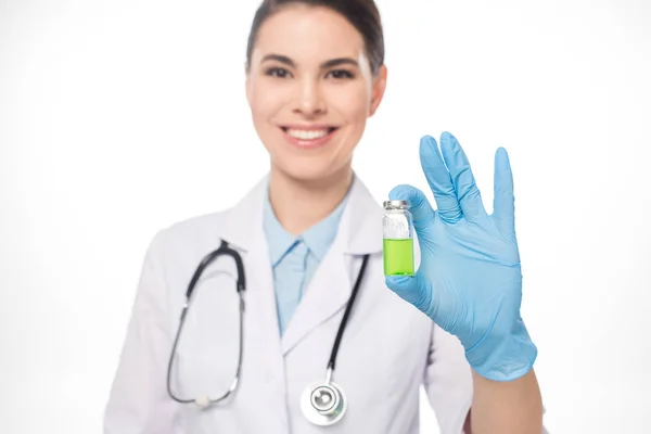 Enfoque selectivo del médico sonriente sosteniendo frasco con vacuna verde aislada en blanco - foto de stock