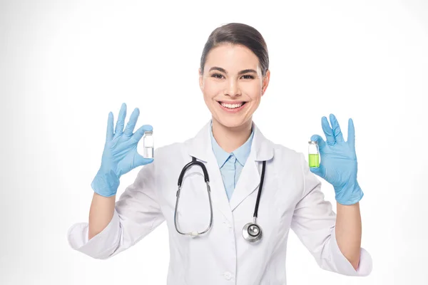 Hermoso médico sonriendo a la cámara mientras sostiene frascos con vacunas aisladas en blanco - foto de stock