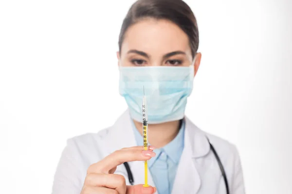 Enfoque selectivo del médico en la jeringa de sujeción de máscara médica aislada en blanco - foto de stock