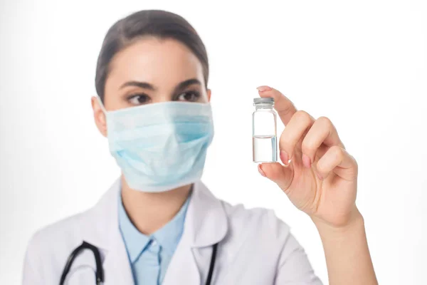 Enfoque selectivo del médico en mascarilla médica sosteniendo frasco con vacuna aislada en blanco - foto de stock