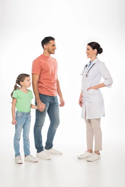 Longitud completa de pediatra femenina sonriendo al padre con hija sobre fondo blanco - foto de stock