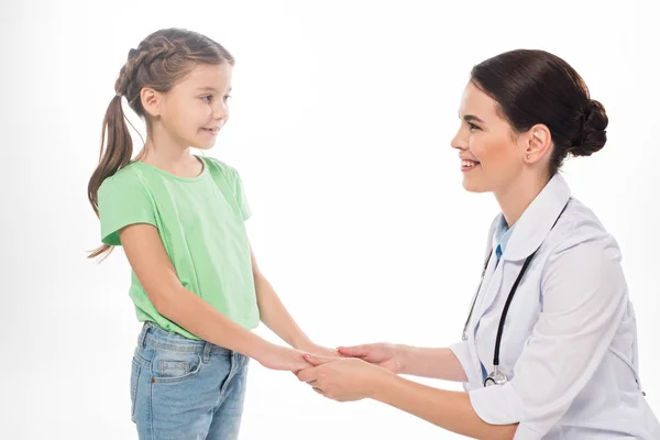 Vista laterale del pediatra e del bambino che si tengono per mano e si sorridono isolati su bianco — Foto stock