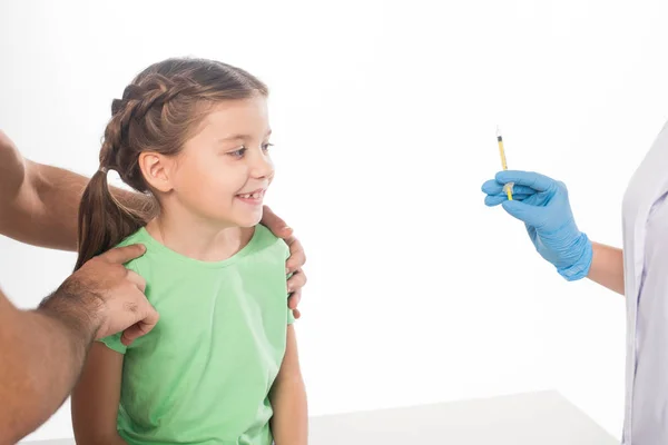 Padre sosteniendo niño sonriente cerca de pediatra con jeringa aislada en blanco - foto de stock