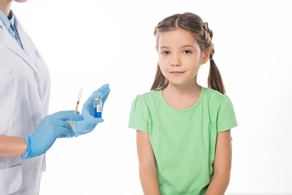 Pediatrician with flu vaccine and syringe near kid looking at camera isolated on white — Stock Photo