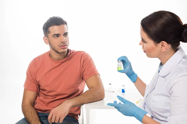 Жінка-лікар, що показує вакцину проти к.с. для пацієнта за столом ізольовано на білому — стокове фото
