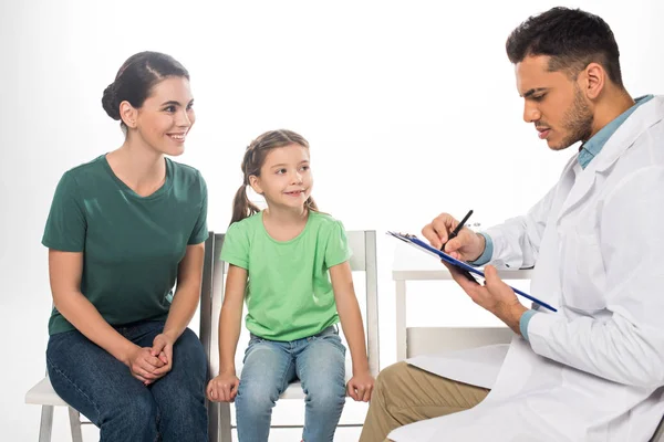 Smiling mother with daughter looking at pediatrician with clipboard isolated on white — Stock Photo