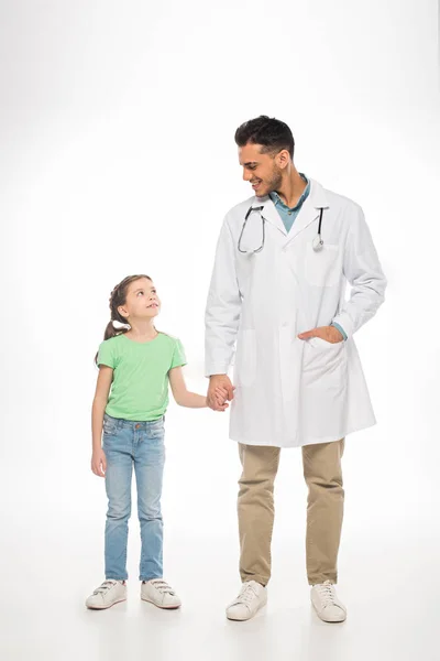 Lunghezza completa del bambino e del pediatra che si sorridono a vicenda e si tengono per mano su sfondo bianco — Foto stock