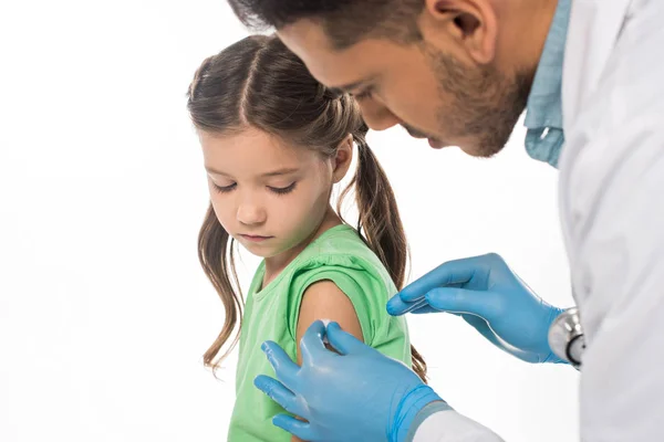 Selective focus of pediatrician rubbing shoulder of child with cotton wool isolated on white — Stock Photo