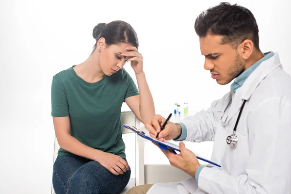 Doctor escribiendo en portapapeles cerca triste paciente en aislado en blanco — Stock Photo