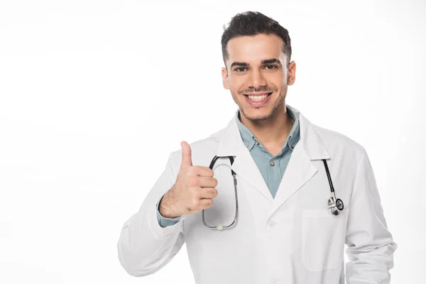 Guapo médico mostrando el pulgar hacia arriba y sonriendo a la cámara aislada en blanco - foto de stock