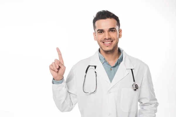 Médico bonito apontando com o dedo e sorrindo para a câmera isolada no branco — Fotografia de Stock