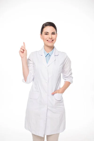 Bella medico sorridente alla fotocamera e puntando con il dito isolato su bianco — Foto stock
