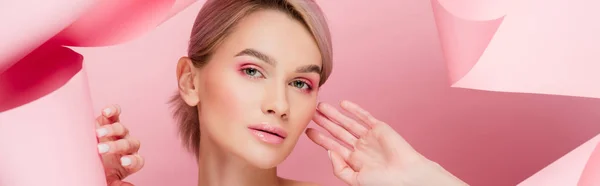 Panoramic shot of beautiful young wwoman with pink makeup in torn paper, on pink — Stock Photo