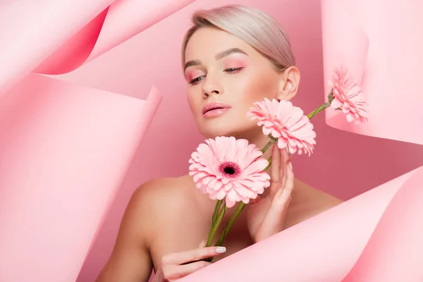 Naked girl with pink flowers and makeup in torn paper, on pink — Stock Photo