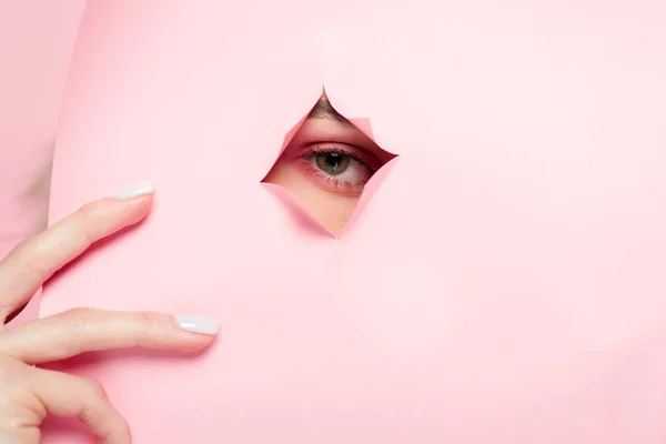 Cropped view of girl with pink makeup looking through torn paper — Stock Photo