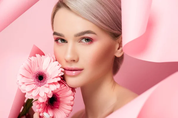 Beautiful girl with pink flowers and makeup in torn paper, on pink — Stock Photo