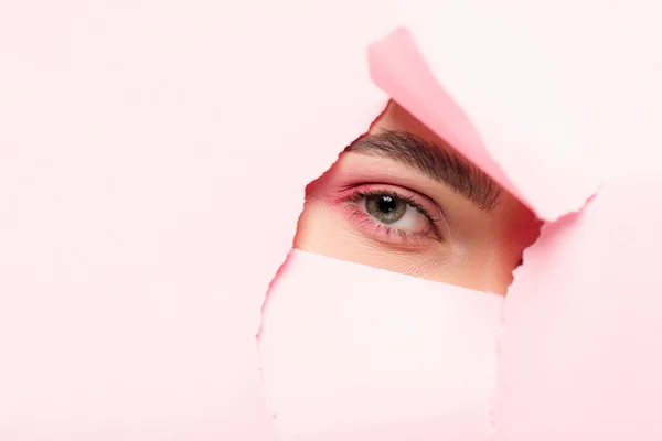 Vista cortada da mulher com maquiagem rosa olhando através de papel rasgado — Fotografia de Stock