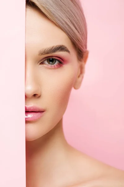 Schönes Mädchen mit perfekter Haut und rosa Make-up posiert mit einem Stück Papier, isoliert auf rosa — Stockfoto