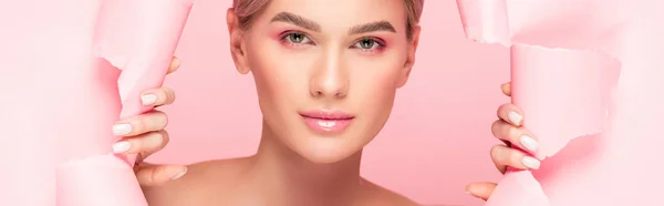 Plano panorámico de tierna mujer con maquillaje rosa en papel roto, aislado en rosa - foto de stock