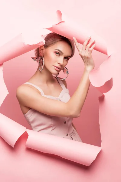 Fashionable girl in pink dress posing in torn paper, on pink — Stock Photo