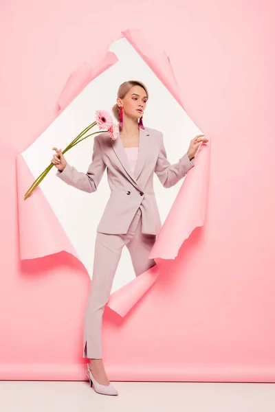 Attractive girl in trendy suit holding flowers and posing in torn paper, on white — Stock Photo