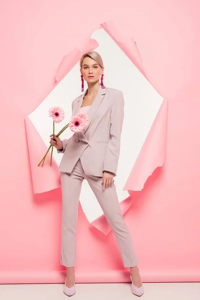 Menina bonita em terno na moda segurando flores e posando em papel rasgado, em branco — Fotografia de Stock