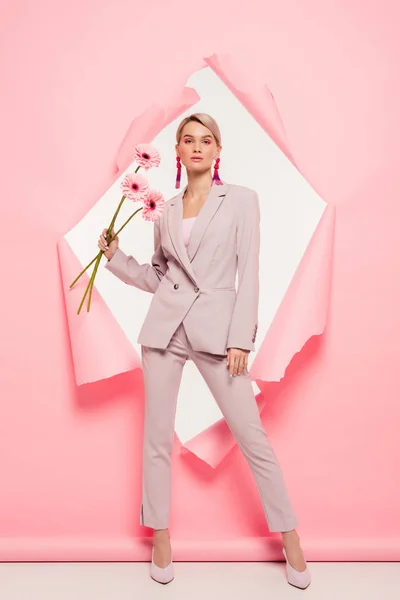 Beautiful girl in fashionable suit holding flowers and posing in torn paper, on white — Stock Photo