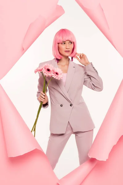 Fashionable girl in suit and pink wig holding flowers and posing in torn paper,  isolated on white — Stock Photo