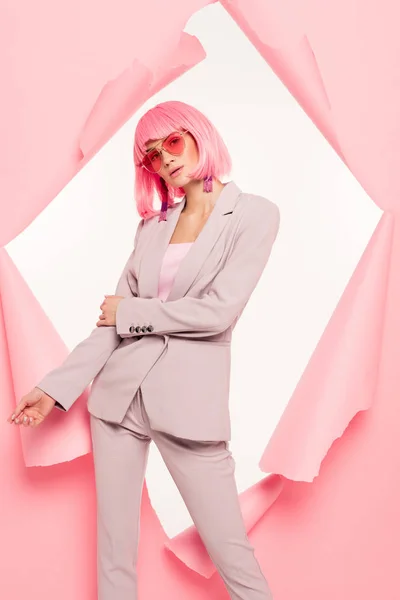 Stylische Frau im Anzug, trendige Sonnenbrille und rosa Perücke posieren in zerrissenem Papier, isoliert auf weiß — Stockfoto