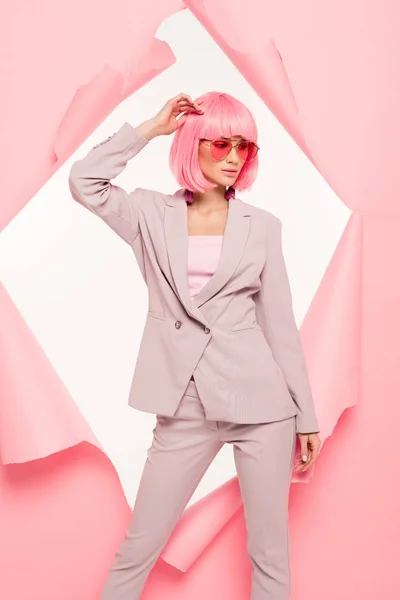 Chica con estilo en traje, gafas de sol y peluca rosa posando en papel roto, aislado en blanco - foto de stock