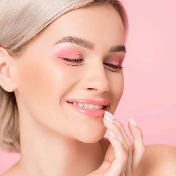 Hermosa chica sonriente con maquillaje rosa tocando los labios, aislado en rosa - foto de stock