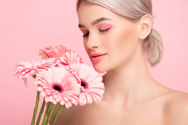 Hermosa chica con los ojos cerrados y maquillaje rosa sosteniendo flores de gerberas, aislado en rosa - foto de stock