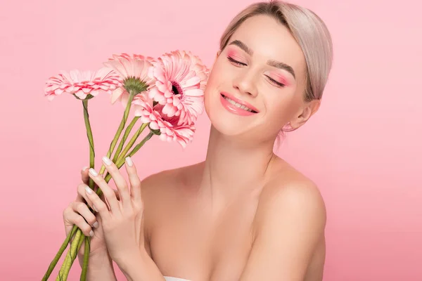 Alegre chica desnuda con maquillaje rosa sosteniendo flores de gerberas, aislado en rosa - foto de stock