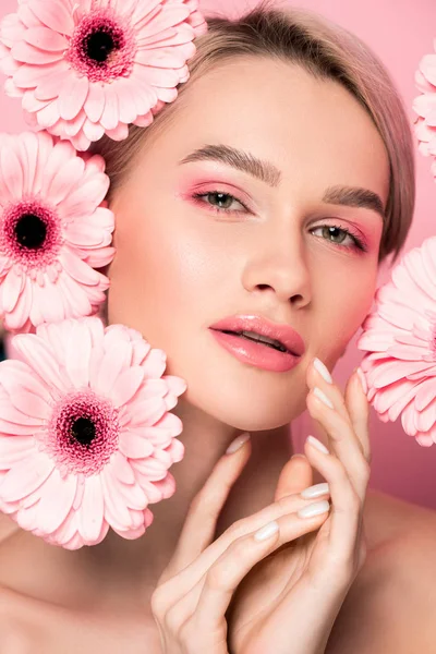 Tenera ragazza con trucco e fiori di gerbera rosa, isolati su rosa — Stock Photo
