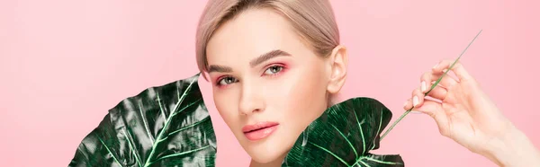 Plano panorámico de chica atractiva con maquillaje rosa aislado en rosa con hojas verdes — Stock Photo